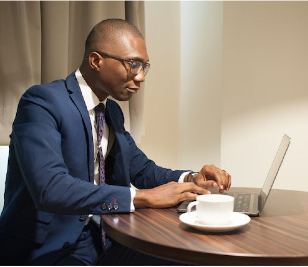 A man black man wearing a blue suit with a laptop before him